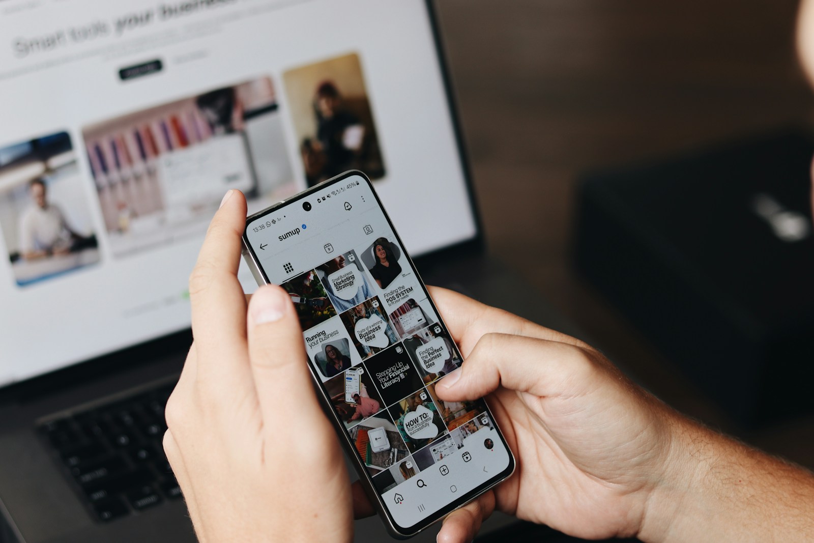 A creator managing social accounts on a phone beside a laptop.